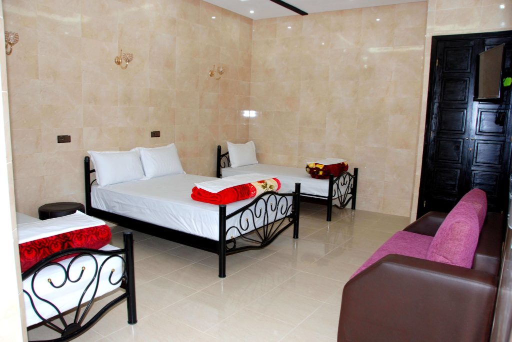 chambre hotel Marrakech pour 4 adultes composée de 1 lit double et 2 lits avec salle de bain privée, TV avec satellite, Wifi, salon avec des canapés